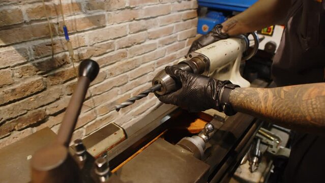 Cropped shot of male tattooed specialist using drilling machine while working in workshop