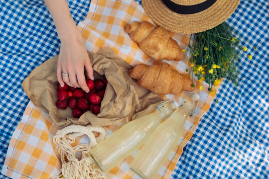 Delightful picnic spread: croissants, strawberries, lemonade on checkered blanket.