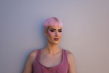 Portrait of young gay boy with pink hair and make-up standing on a white background and making different expressions with his face. Concept of equality and LGBTQ rights.