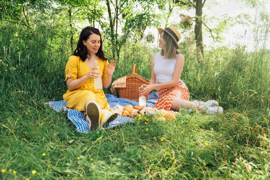 Pair of women sipping lemonade from bottles on blue picnic blanket.
