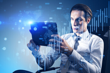 Attractive young businessman sitting and using tablet with growing blue forex chart and map...