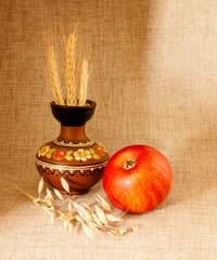 Still life with an apple, a clay jug with ears of wheat, against a background of natural linen.