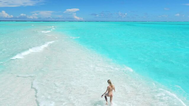 Woman in swimsuit running on sandbank with turquoise ocean. Aerial view with girl on her vacation in tropics