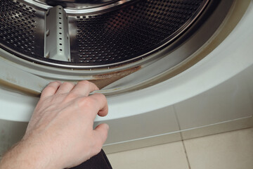 Dirty moldy washing machine sealing rubber. The person checks the dirt on the rubber of a washing machine. Cropped hand holding washing machine.