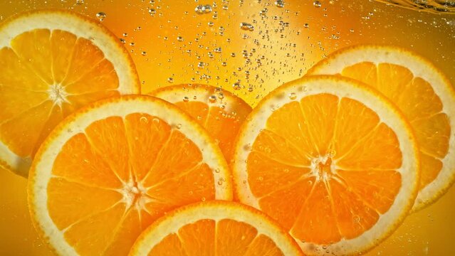Super Slow Motion Shot of Fresh Orange Slices Floating and Rising in Sparkling Water at 1000 fps.