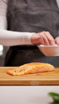 Person seasoning salmon on wood cutting board with fingers