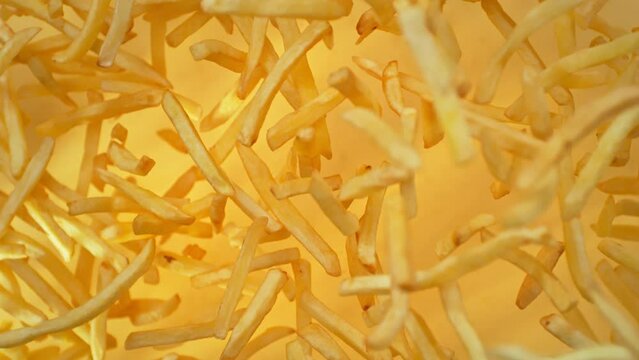 Super Slow Motion Shot of French Fries Flying Towards Camera on Golden Background at 1000fps.
