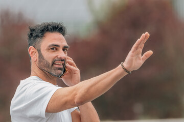 attractive young adult man with beard outdoors talking on mobile phone and waving