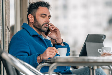 attractive young adult man with beard drinking coffee with mobile phone and tablet