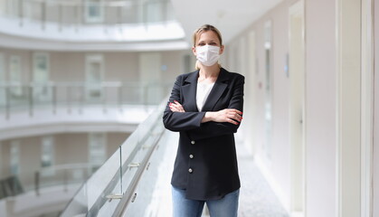 Young woman in suit and protective medical mask standing in corridor of hotel. Hotel customer...