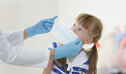 Doctor putting protective medical mask on little girl in clinic. Prevention covid19 mask mode...