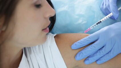Nurse giving injection in shoulder of young woman in clinic closeup. Vaccination against covid 19...