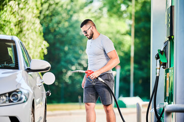 Driver with gasoline pump refilling car gas tank. Confident man refueling his luxury white auto....