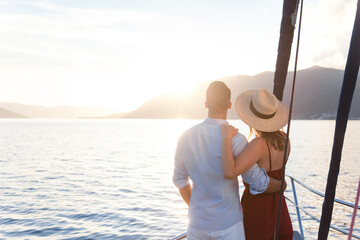 Traveling on yacht. Happy couple in love enjoying sunset and summer vacation by sea. Young travelers relaxing. Intimate romantic date on sailboat, rear view. Trip, holidays with beautiful landscape.