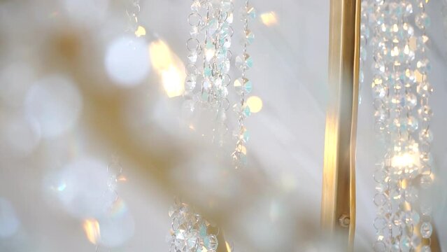 Elegant light crystal chandelier details on party people blurred silhouettes, close-up. Warm multi-colored lights and reflections on transparent glass. Slow movement.