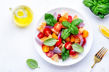 Italian salad with tomatoes, stale bread, red onion, olive oil, salt and green basil, white table background, top view