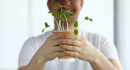 Smiling man hold pot with green shoots closeup. Home gardening concept.