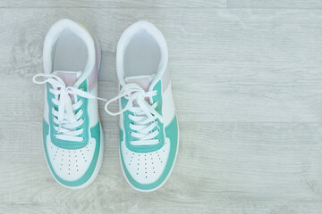 White sneakers with green and pink accents on a wooden floor. View from above.