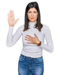 Beautiful brunette woman wearing casual clothes swearing with hand on chest and open palm, making a...