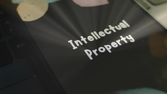 Intellectual Property inscription on smartphone screen. Graphic presentation on black background with bokeh lights. Light rays. Legal concept