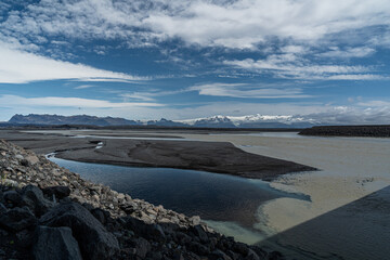 Unmittelbar neben der Ringstraße in Island befinden sich schwarze Lavafelder, Wasser und Geröll von den Gletschern im Hintergrund