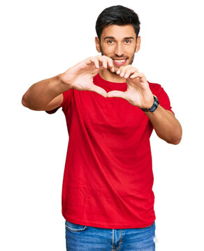 Fototapeta Young handsome man wearing casual red tshirt smiling in love doing heart symbol shape with hands. romantic concept.