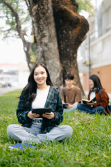 Asian Students are studying the campus park. Young people are spending time together. Reading book, working with laptop and tablet