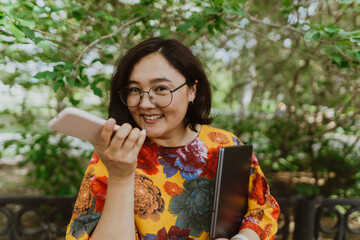 Cheerful young woman with glasses talking on a mobile phone in a lush green park. Business lady professional talking on mobile while enjoying nature