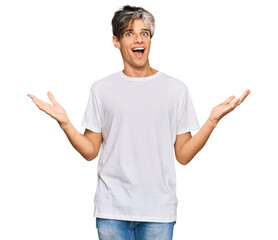 Young hispanic man wearing casual white tshirt celebrating victory with happy smile and winner expression with raised hands