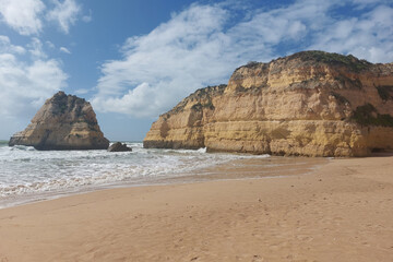 Fototapeta na wymiar Rocky sea stacks on sandy beach with waves crashing.