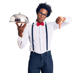 Handsome african american man with afro hair wearing waiter uniform holding silver tray with angry...