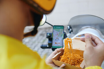 Motorbike taxi driver checking requests on smartphone when eating lunch