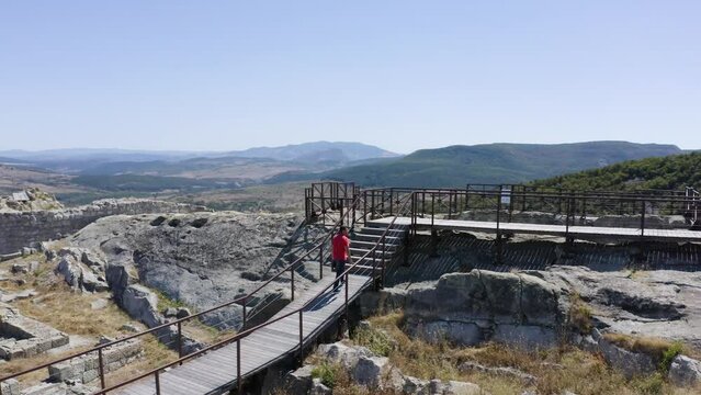 Orbiting drone shot showing a man walking towards a water reservoir through a ramp of wooden planks on top of the ancient city of Perperikon in the province of Kardzhali in Bulgaria.