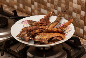 Fried fish on a white plate on the gas stove in the kitchen