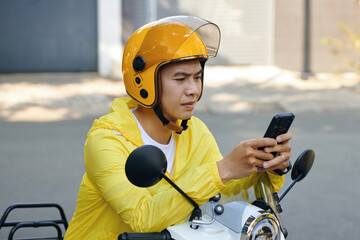 Frowning motorbike taxi driver checking request notifications on smartphone