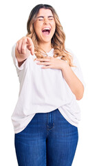 Young caucasian woman wearing casual clothes laughing at you, pointing finger to the camera with hand over body, shame expression