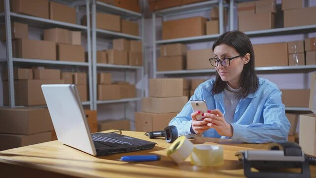 Portrait of a positive young woman warehouse worker using a phone at work