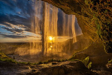 Die Mitternachtssonne scheint durch den Wasserfall Seljalandsfoss, Wasserfall von hinten fotografiert
