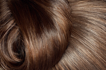 A closeup view of a bunch of shiny brown hair in a wavy curved style. Brown hair background