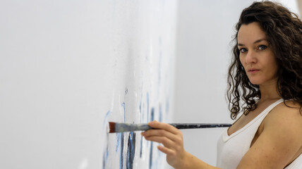 sexy beautiful pretty mature artist woman female painter with curly brunette hair in white casual underskirt paints with Brush an artwork on the studio wall