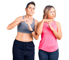 Couple of women wearing sportswear doing time out gesture with hands, frustrated and serious face