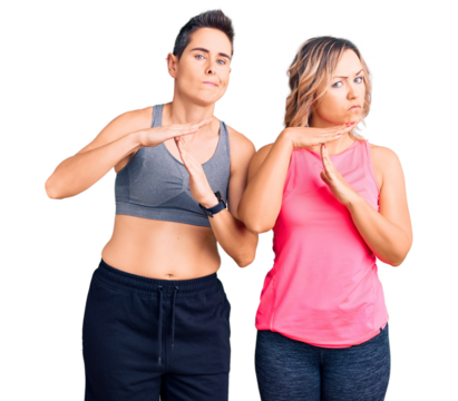 Couple of women wearing sportswear doing time out gesture with hands, frustrated and serious face