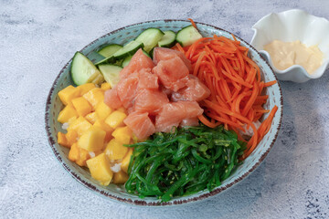 Salmon Poke with mango and wakame seaweed in blue ceramic bowl, on gray background