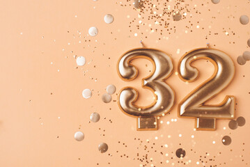 32 years celebration. Greeting banner. Gold candles in the form of number thirty one on peach background with confetti.