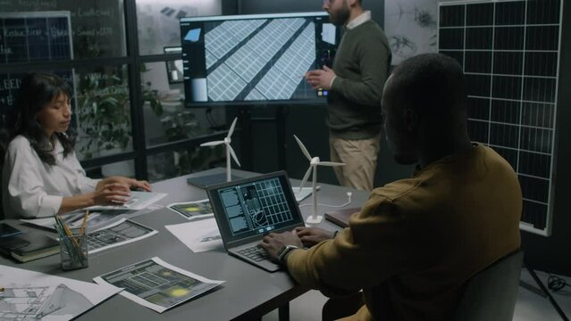 Full medium footage of male Biracial renewable energy specialist presenting enhanced solar panel layout on multimedia screen to diverse partners during clean energy business conference
