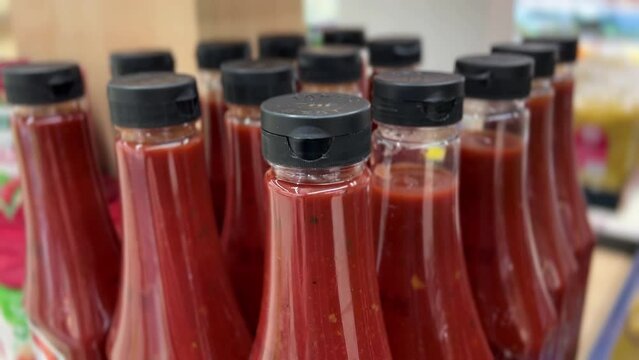 Many of Ketchup bottles on shelf in supermarket. Close-up. Buyer's hand taking tomato sauce from store shelf