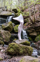 artistic photo of young sexy elegant nude woman, her body wrapped in long skin tight white dress highlighting body shapes, a living statue in nature waterfalls on stone rock