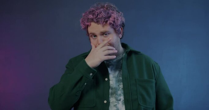 Slow motion portrait of ashamed young man doing face palm hand gesture hiding face and shaking head on purple background. Emotion and expression concept.