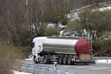 A tanker truck barrels down a sunlit highway, its gleaming white and blue body catching the eye.