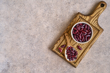 Red kidney beans in ceramic bowl and spoon on wooden board. Top view